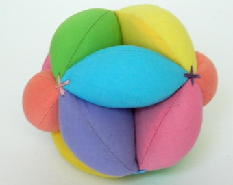 May include: A colorful, soft fabric ball with a unique design. The ball features segments in various colors, including green, yellow, blue, pink, orange, and purple. Each segment is stitched together, creating a visually appealing and tactile toy.