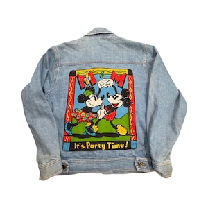 May include: A light blue denim jacket featuring a large, colorful graphic on the back. The design depicts two cartoon mice dancing inside a rectangular frame with the text M&M and It's Party Time! in yellow and red against a blue background.