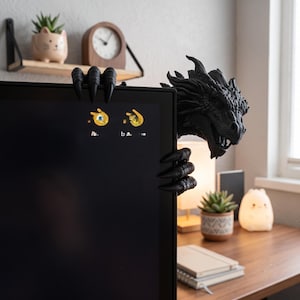 Detailed close-up of a fantasy dragon head gripping the corner of a computer monitor. The dark metallic-brown sculpture features layered facial scales, long pointed horns, textured skin, a strong snout and curved claws, creating dramatic gamer desk decor and a unique screen-top companion.