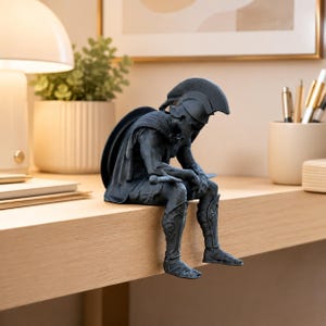 Könnte beinhalten: Eine mattschwarze Figur eines sitzenden Kriegers mit Kammhelm und Rüstung, der ein Schwert auf dem Schoß hält. Die Figur ist in einer nachdenklichen Pose mit gesenktem Kopf dargestellt und zeigt detaillierte Beinschienen sowie einen Umhang.