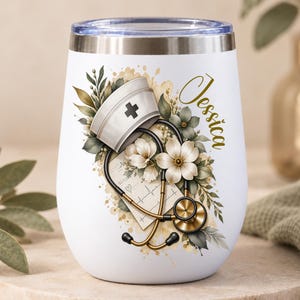 May include: A white stainless steel tumbler featuring a graphic of a nurse cap, a stethoscope, a heart rhythm chart, and flowers. The name Jessica is printed in gold script on the side. The tumbler has a clear lid and a metallic rim.