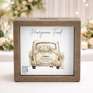 May include: A wooden box with a slot on top, featuring a printed image of a vintage car decorated with flowers and the text "Honeymoon Fund." The car has a "Just Married" sign and the couple's name. A QR code is visible on the bottom left.