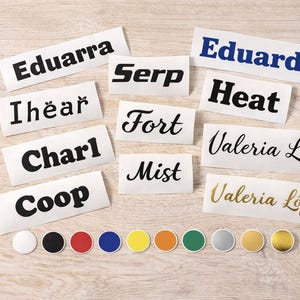 Könnte beinhalten: Eine Sammlung von Namensschildern mit verschiedenen Namen in unterschiedlichen Schriftarten und Farben. Die Namen umfassen "Eduarra", "Serp", "Iheär", "Charl", "Coop", "Fort", "Mist", "Heat", "Eduardo" und "Valeria López". Außerdem sind mehrere farbige runde Aufkleber vorhanden.