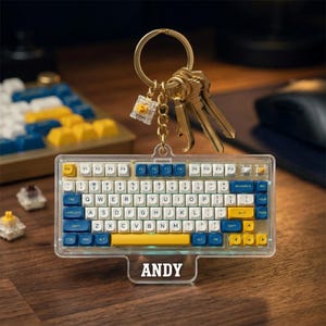 May include: A clear acrylic keyboard keychain with white, blue, and yellow keys, attached to a gold keyring with keys. The keychain has the name "ANDY" printed on the bottom. The keyboard design is a miniature replica of a mechanical keyboard.