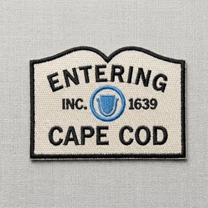 May include: Embroidered patch with a cream background and black border. The patch reads "ENTERING CAPE COD" with "INC. 1639" and a blue emblem. The patch is rectangular with a unique top shape.