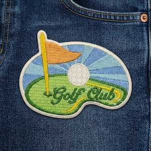 May include: Embroidered patch featuring a golf scene with a white golf ball, orange flag, and the words "Golf Club" in green and yellow. The patch is set against a blue sky and green grass, with a white border.