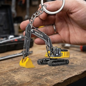 May include: A yellow and black excavator keychain with the name "MASON" printed on the arm. The keychain is made of metal and has a silver key ring.