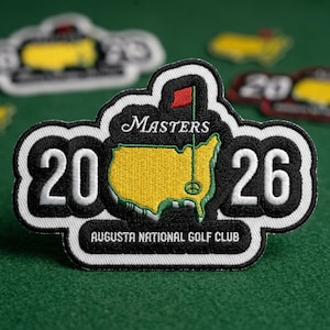 May include: Embroidered patch featuring the Masters logo with a yellow map of the course, a red flag, and the text "Masters 2026 Augusta National Golf Club." The patch has a black and white border and is on a green surface.