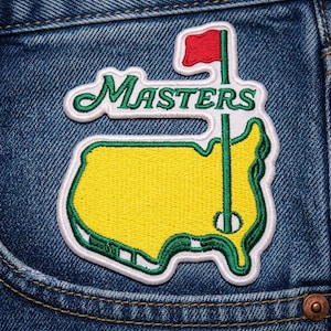May include: Embroidered patch featuring the word "Masters" in green script above a yellow and green outline of a golf course map with a red flag. The patch is sewn onto blue denim.