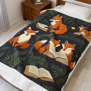 Könnte beinhalten: Eine dunkelblaue Decke mit Illustrationen von orangefarbenen Füchsen, die Bücher lesen. Die Füchse sind von grünen, farnartigen Blättern und kleinen gelben Sternen umgeben. Die Decke liegt auf einem Bett mit einem weißen Kissen.