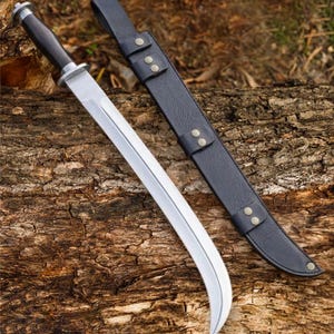 Könnte beinhalten: Ein Messer mit geschwungener Stahlklinge, dunklem Holzgriff und silbernem Knauf, dazu eine schwarze Lederscheide mit Metallnieten und Gürtelschlaufe. Das Messer hat eine polierte Oberfläche und eine deutlich geschwungene Schneide.