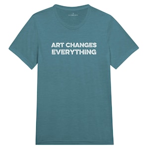 May include: Teal-colored t-shirt with the text "ART CHANGES EVERYTHING" in white, distressed lettering. The shirt has a crew neck and short sleeves. The brand name "FEATHER GIFTS" is printed at the top.