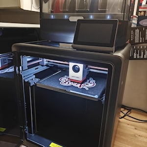 Op de afbeelding: Een donkergrijze 3D-printer met een transparante filamentbehuizing aan de bovenkant met meerdere spoelen. De printer is voorzien van een touchscreen aan de voorzijde, een printkop met het label ANYCUBIC en een getextureerd printbed.