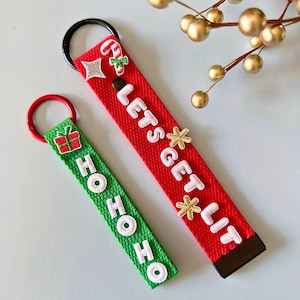 May include: Two Christmas-themed keychains. One is red with the text "LET'S GET LIT" and festive embellishments. The other is green with "HO HO HO" and a gift graphic. Both have metal key rings.
