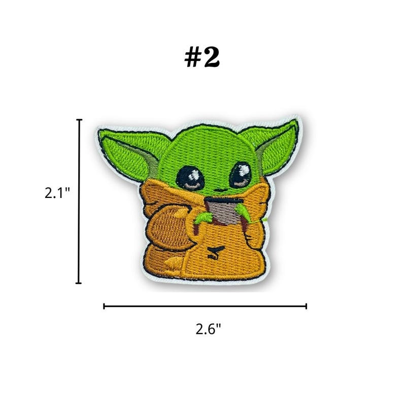 May include: Embroidered patch featuring a green alien character with large ears and black eyes, wearing a tan robe. The patch is 2.1 inches tall and 2.6 inches wide, with the number "#2" above the character.