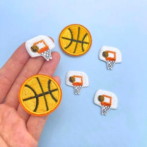 May include: A collection of embroidered patches featuring basketballs and basketball hoops. The basketball patches are round with yellow and black details and orange borders. The basketball hoop patches are white with orange rims.