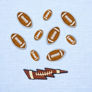 May include: A collection of embroidered patches featuring eight brown American footballs with white stitching and one brown lightning bolt patch with white stitching and a dark blue border, all arranged on a light blue fabric surface.