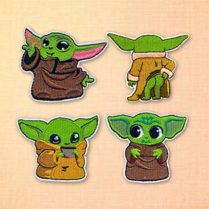 May include: Four embroidered patches featuring a green alien character with large eyes and pointed ears. The character is depicted in various poses, wearing brown and tan robes. The patches have a white border and are set against a light orange background.