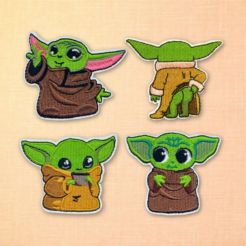 May include: Four embroidered patches featuring a green alien character with large eyes and pointed ears. The character is depicted in various poses, wearing brown and tan robes. The patches have a white border and are set against a light orange background.