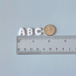 May include: White embroidered letters 'ABC' with a ruler showing measurements in inches. A US dime is next to the letters for size comparison. The letters are approximately 0.75 inches tall.