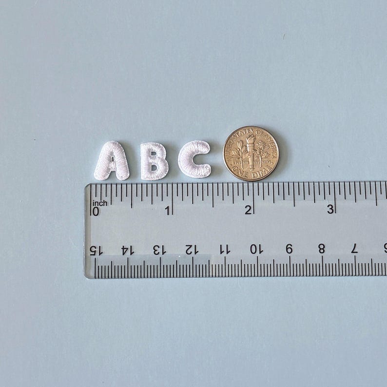 May include: White embroidered letters 'ABC' with a ruler showing measurements in inches. A US dime is next to the letters for size comparison. The letters are approximately 0.75 inches tall.