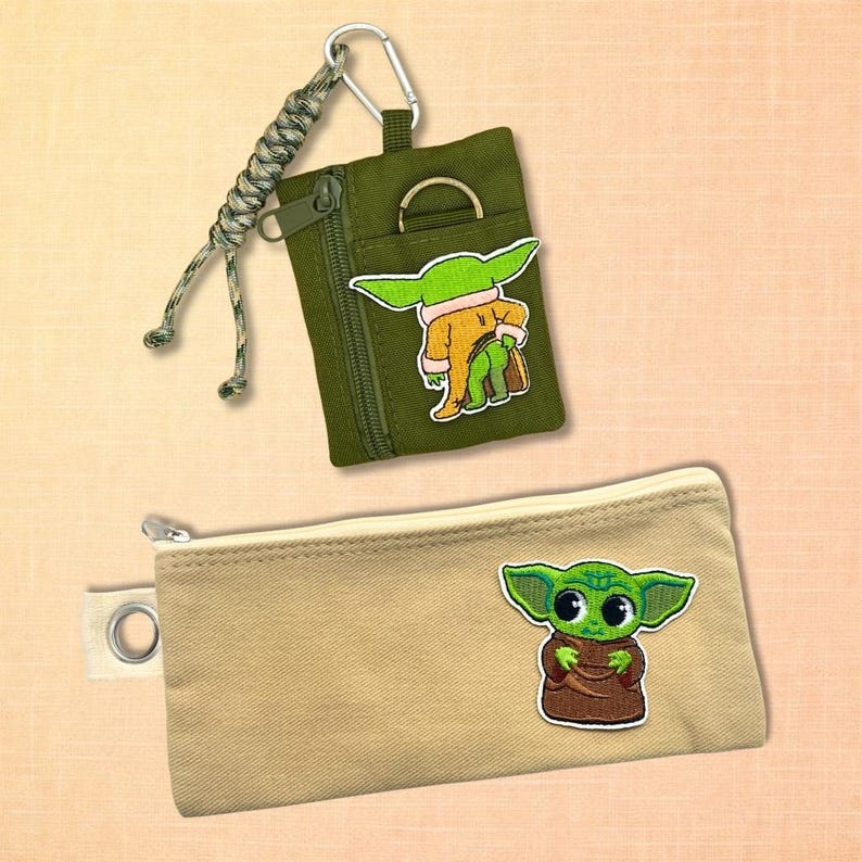 May include: Two small zippered pouches. One is olive green with a silver zipper and a cartoon character patch. The other is tan with a silver zipper and a cartoon character patch. Both pouches have a cartoon character patch.