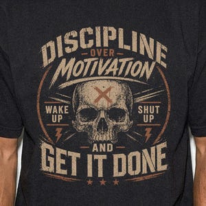 May include: Black t-shirt with a distressed graphic design. The design features a skull, the words "DISCIPLINE OVER MOTIVATION," and the phrases "WAKE UP" and "SHUT UP." Below the skull, the text reads "AND GET IT DONE."
