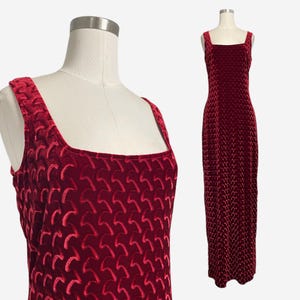 May include: A burgundy velvet dress with a square neckline and wide straps. The dress features a repeating pattern and is displayed on a mannequin. The floor-length gown is a formal wear item.