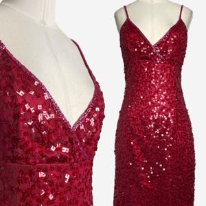 May include: A knee-length, sleeveless dress in a deep magenta hue, fully covered in square-shaped sequins. The garment features a V-neckline with thin spaghetti straps and a fitted bodice that transitions into a straight skirt silhouette.