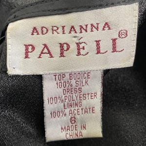 K&ouml;nnte beinhalten: Nahaufnahme eines Etiketts von einem Adrianna Papell Kleid. Das wei&szlig;e Etikett hat burgunderfarbenen Text, der die Zusammensetzung des Kleides auflistet: 100 % Seide f&uuml;r das Oberteil, 100 % Polyester f&uuml;r das Futter und 100 % Acetat. Das Etikett gibt auch die Gr&ouml;&szlig;e 6 und Made in China an.