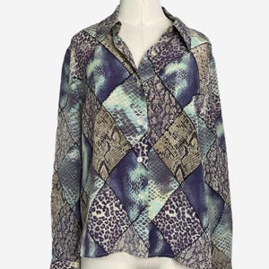May include: A long-sleeved button-down shirt with a patchwork design. The shirt features a variety of animal print patterns in shades of blue, purple, and tan. The shirt is displayed on a mannequin.