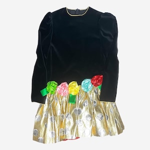 May include: A black velvet dress with a gold and silver polka dot skirt. The dress has a round neckline and long sleeves. The skirt is adorned with colorful satin rosettes.