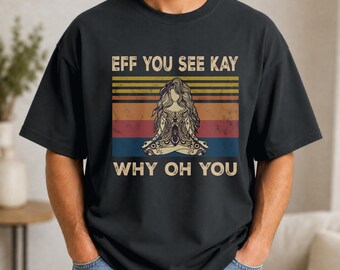May include: A black t-shirt featuring a graphic print of a person in a lotus yoga pose. The design includes horizontal stripes in yellow, orange, red, and blue, with the text "EFF YOU SEE KAY" above and "WHY OH YOU" below the central figure.