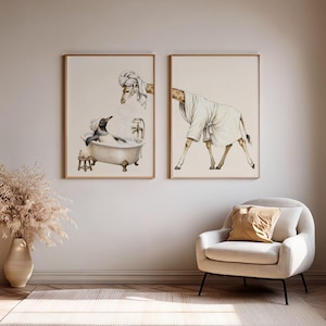 Peut inclure: Deux cadres muraux illustrant des animaux. L'image de gauche montre un manchot dans une baignoire avec une girafe portant une serviette sur la tête. L'image de droite représente une girafe vêtue d'un peignoir blanc, sur des fonds couleur crème.