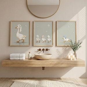 May include: Three framed prints featuring watercolor illustrations of geese in a bathroom setting. One print shows a goose with a towel on its head, another shows three geese, and the last shows a running goose with a blue hat.