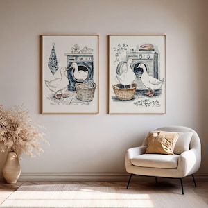 Pode incluir: Dois quadros de parede com ilustrações detalhadas a tinta de patos brancos numa lavandaria. Os desenhos mostram patos a interagir com máquinas de lavar e cestos de vime, representados em tons de azul, castanho e branco.