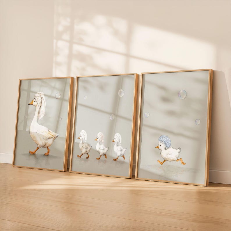 May include: Set of three framed art prints featuring whimsical illustrations of geese and ducklings. The artwork depicts a goose with a towel on its head, and ducklings wearing shower caps. The prints have a light green background and wooden frames.