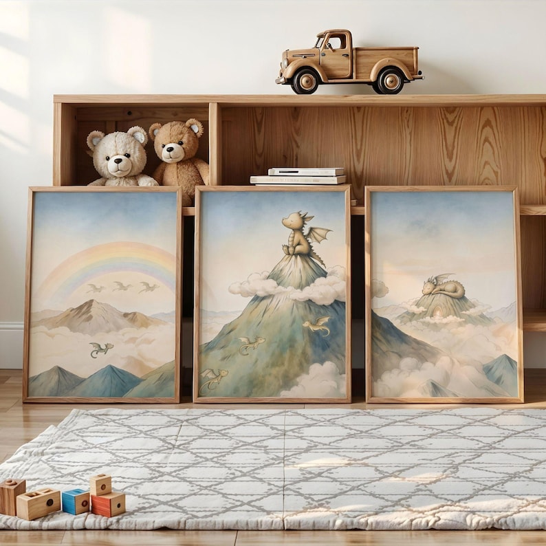 May include: Three framed art prints with watercolour illustrations of dragons in a mountain landscape. One print shows a rainbow, another a dragon on a cloud, and the third a sleeping dragon. The frames are light brown.