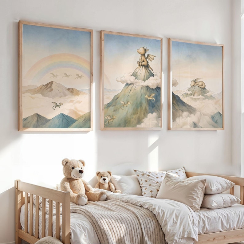 May include: Three framed watercolour prints with a whimsical dragon theme. The artwork features dragons, mountains, rainbows, and clouds in soft pastel colours. The prints are displayed above a wooden bed with teddy bears and pillows.
