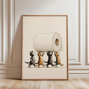 Pode incluir: Uma impressão de arte emoldurada apresentando uma ilustração caprichosa de quatro gatinhos em tons de cinza, laranja e preto, caminhando em fila enquanto carregam coletivamente um grande rolo de papel higiênico branco sobre suas cabeças.