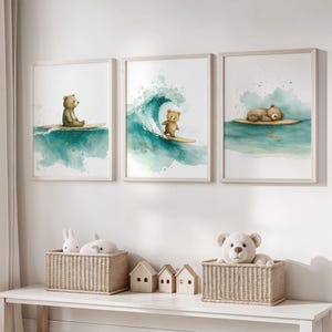 Könnte beinhalten: Drei gerahmte Aquarelldrucke mit surfenden Teddybären. Die Drucke haben einen hellen Holzrahmen und zeigen Bären auf Surfbrettern in einem türkisfarbenen Ozean. Der erste Bär sitzt, der zweite reitet eine Welle und der dritte liegt.