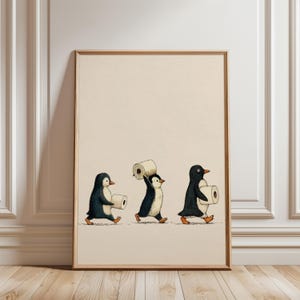 May include: A framed wall art print on a light beige background featuring three illustrated penguins walking in a line. Each penguin is black and white with orange feet and beaks, and each is carrying a single roll of white toilet paper.