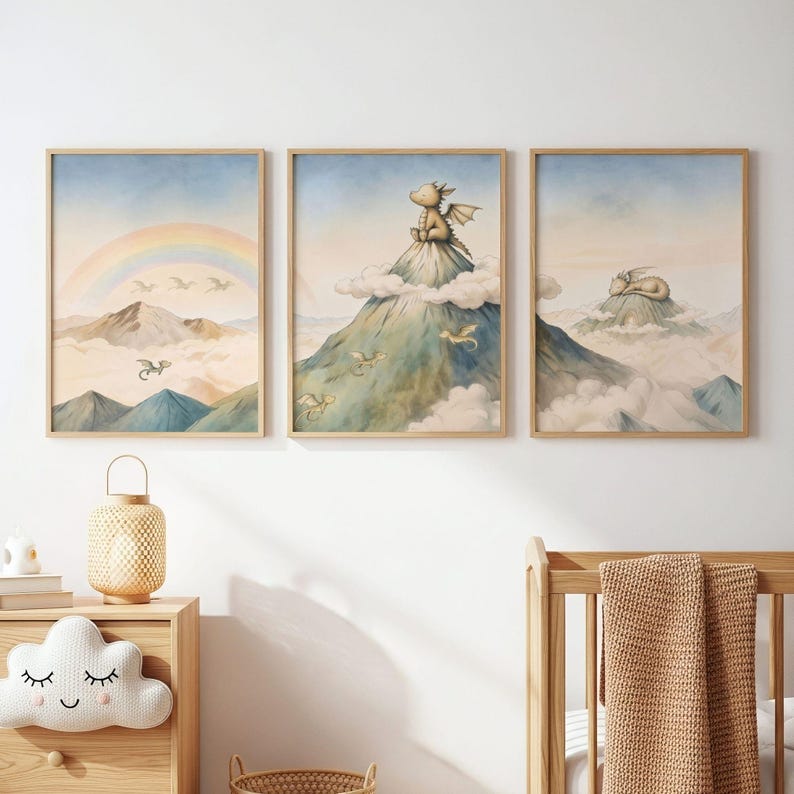 May include: Three framed art prints with watercolour illustrations of dragons in a fantasy landscape. One print shows a rainbow, another a dragon on a mountain, and the third a sleeping dragon. The prints are in light wood frames.