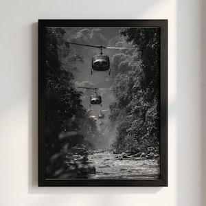 Può includere: Una stampa artistica da parete incorniciata in bianco e nero che raffigura una formazione di tre elicotteri militari in volo in linea attraverso una stretta e fitta valle della giungla sopra un ruscello roccioso, in una cornice di legno scuro.