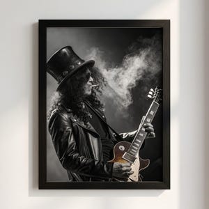 Pode incluir: Uma impressão artística emoldurada a preto e branco apresentando um músico com cabelo comprido e encaracolado, usando uma cartola e um casaco de cabedal, a tocar uma guitarra elétrica enquanto fuma. A imagem tem um estilo esfumado.