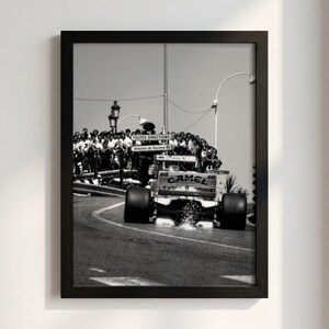 Peut inclure: Une photographie encadrée en noir et blanc d'une voiture de course de Formule 1 sur une piste. La voiture porte l'inscription CAMEL sur l'aileron arrière. Une foule de spectateurs se tient derrière une barrière avec des panneaux TOUTES DIRECTIONS.