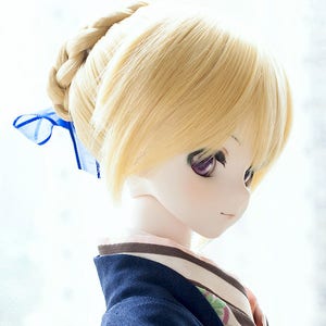 Puede incluir: Una mu&ntilde;eca con el pelo largo y rubio, recogido en una trenza y atado con una cinta azul. La mu&ntilde;eca lleva un kimono azul oscuro con un cuello de rayas blancas y marrones y un estampado floral. La mu&ntilde;eca est&aacute; mirando hacia un lado.