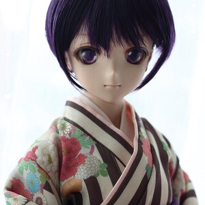 Puede incluir: Una mu&ntilde;eca con cabello morado que lleva un kimono japon&eacute;s tradicional con un patr&oacute;n floral y una faja morada. El kimono tiene rayas marrones y blancas. La mu&ntilde;eca tiene ojos morados y un tono de piel claro.