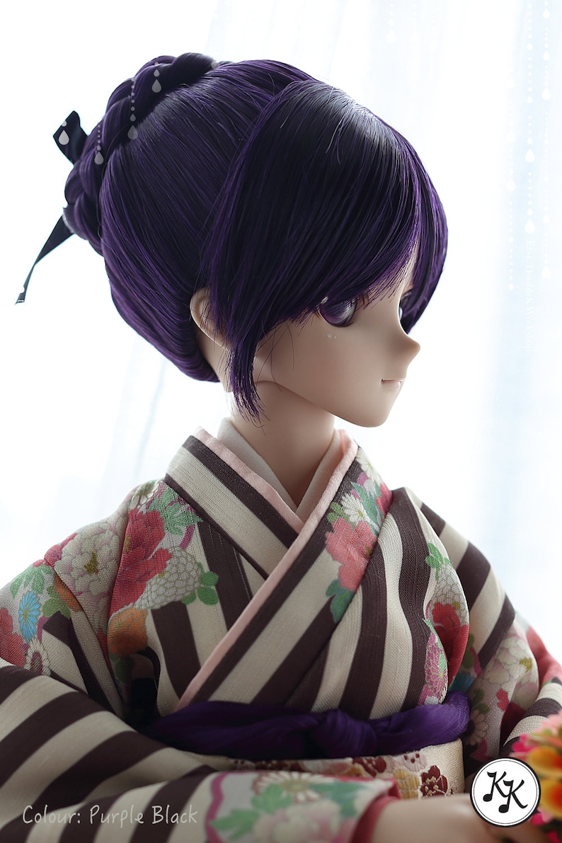 Puede incluir: Una mu&ntilde;eca con el pelo largo y morado oscuro recogido en un mo&ntilde;o con una cinta negra. La mu&ntilde;eca lleva un kimono japon&eacute;s tradicional con un estampado de rayas blancas y marrones y detalles florales. El kimono tiene una faja morada. Los ojos de la mu&ntilde;eca est&aacute;n cerrados.