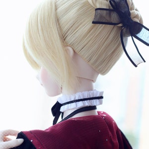 Puede incluir: Una peluca rubia para mu&ntilde;eca, con un estilo de mo&ntilde;o trenzado con una cinta negra. La peluca la lleva una mu&ntilde;eca con un cuello blanco y negro y un vestido rojo.